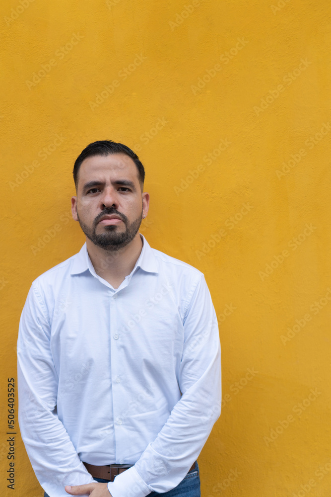 Young man standing in front of a yellow wall. He is looking at the camera serious Young man standing in front of a yellow wall. He is looking at the camera serious