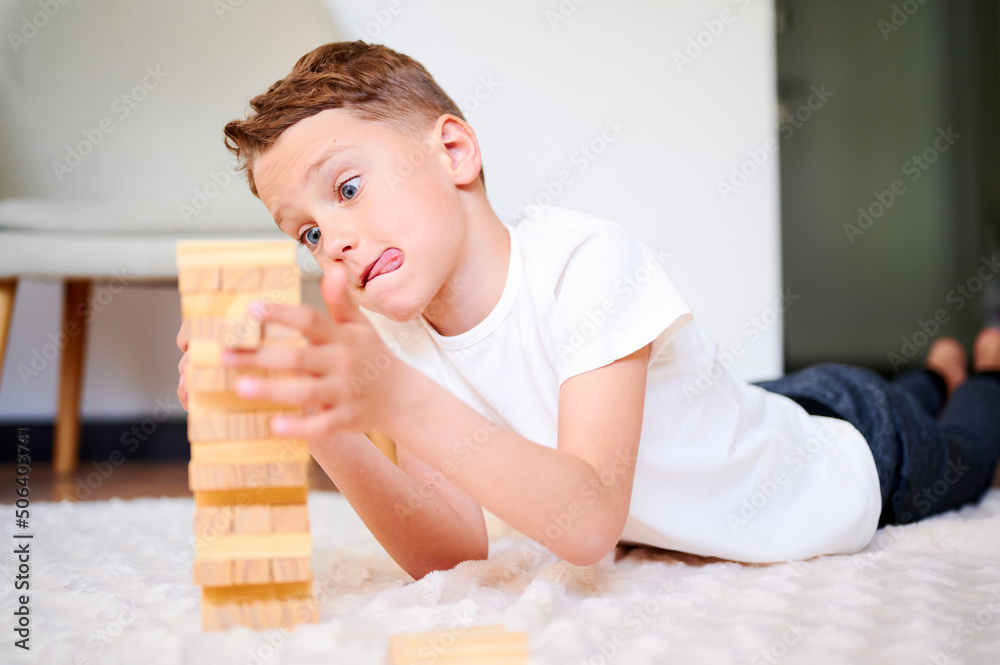 Boy playing wooden block removal tower game at home. Board game. Kids leisure concept. Boy playing wooden block removal tower game at home. Board game. Kids leisure concept.