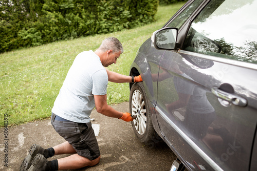 Middle aged man with grey hair changes tires on his family car van © epiximages