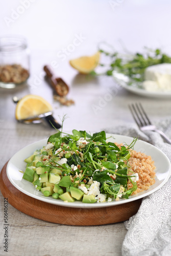 Gluten-free green vegetarian salad made of microgreen sprouts peas, avocado, quinoa, spinach, seasoned  crushed almonds with slices of feta cheese