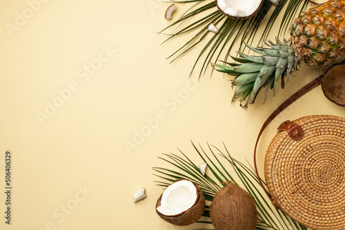 Summer holidays concept. Top view photo of round rattan handbag fresh tropical fruits cracked coconuts pineapple and green palm leaves on isolated beige background with empty space