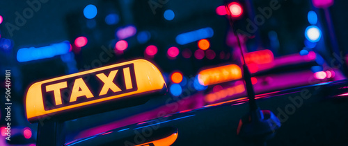 taxi sign in front of colourful city lights at night