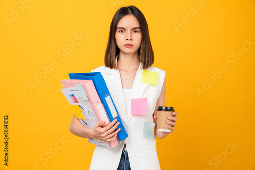 Boring young Asian woman holding document file with coffee cup and a sticky note on the shirt, stand on studio shot yellow background.