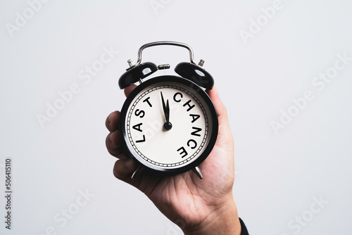 Hand holding black alarm clock which inside last chance wording for time and opportunity concept.