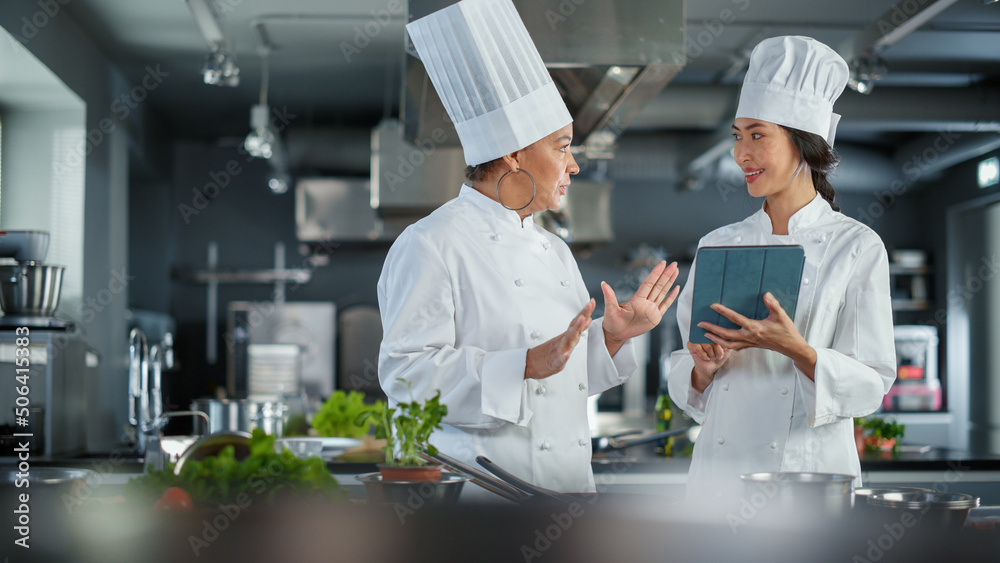 Restaurant Kitchen: Team of Asian and Black Female Chefs use Tablet Computer while Cooking Delicious and Authentic Food. Perfect Teamwork in Preparing Healthy Meal, Fusion Cuisine Dish