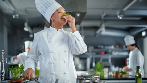 Black Female Chef Takes Fresh Herb, Smells It with a Smile, Secret Ingredient that Makes Grandmother's Recipe Special. Traditional Restaurant Kitchen with Authentic Dish, Healthy, Nurturing Food photo