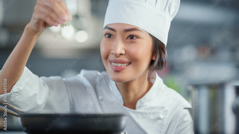 Restaurant Kitchen: Portrait of Asian Female Chef Fries Uses Pan, Seasons Dish with Herbs and Spices, Smiles. Professional Cooking Delicious and Traditional Authentic Food. Healthy Dish Preparation Restaurant Kitchen: Portrait of Asian Female Chef Fries Uses Pan, Seasons Dish with Herbs and Spices, Smiles. Professional Cooking Delicious and Traditional Authentic Food. Healthy Dish Preparation