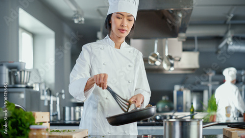 Restaurant Kitchen: Portrait of Asian Female Chef Stirs Her Favourite most Flavourful Dish, Smiles. Professional Cooking Delicious and Traditional Authentic Food. Healthy Dish Preparation. Low Angle