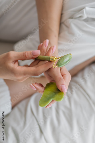 Fototapeta Naklejka Na Ścianę i Meble -  Green jade and gua sha in female hands. Facial massage