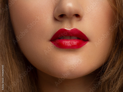 The macro photo of the closed female mouth. Chubby lips with red lipstick show a fashionable make-up and increase in lips. Cosmetology  Spa  cosmetics