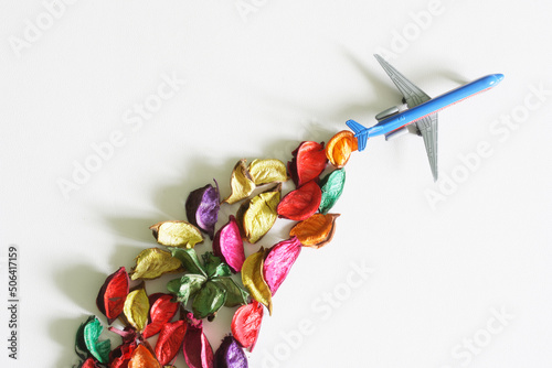 Toy blue passenger airliner with a contrail of colorful flower petals. Concept of eco-friendly biofuel  alternative energy and green revolution. White background. Copy space.