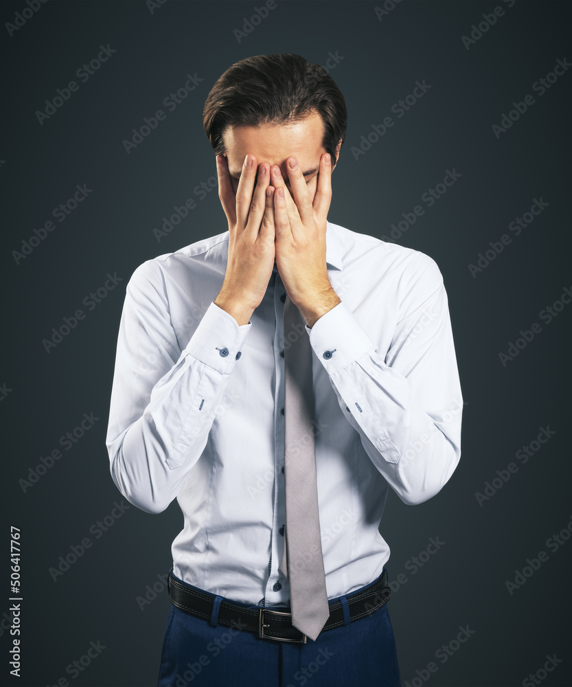 Stress and find solution concept with man in white shirt closing his eyes, facepalm isolated on dark grey background Stress and find solution concept with man in white shirt closing his eyes, facepalm isolated on dark grey background