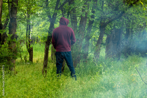 Unrecognized man in hoody peeing near tree in forest