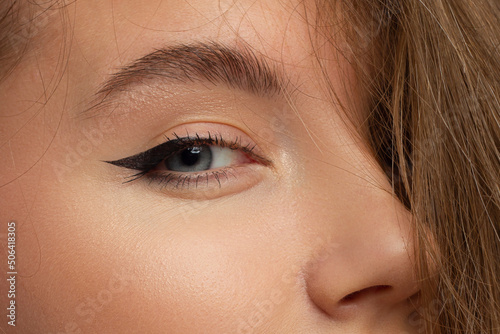 Glamour close-up portrait of beautiful woman model face with winged black eyeliner make-up, clean skin on white background. Long eyelashes and thick eyebrows.