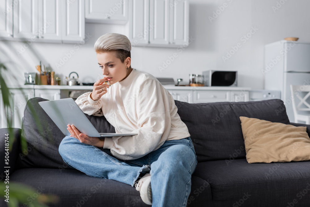 thoughtful woman in white pullover sitting on sofa and looking at laptop thoughtful woman in white pullover sitting on sofa and looking at laptop