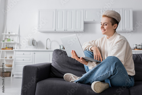 Foto happy woman looking at laptop while sitting on couch with crossed legs