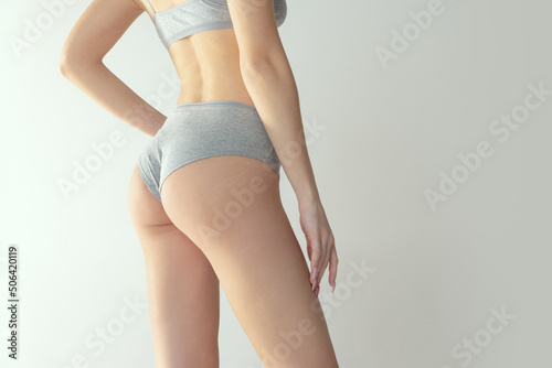 Cropped image of fit, tonned female body, buttocks in comfortable cotton underwear isolated over grey studio background