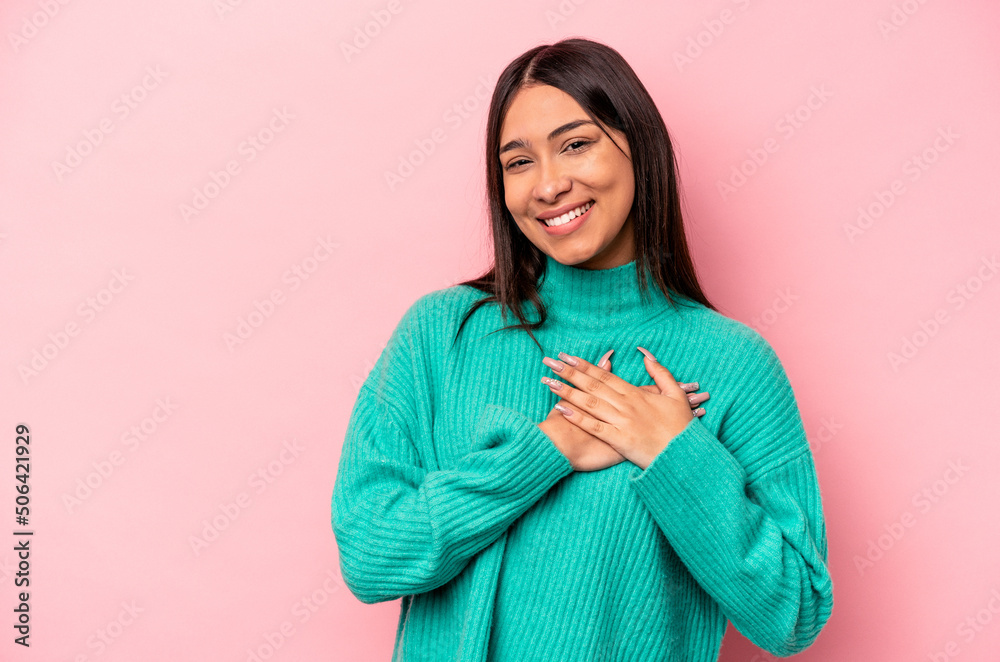 Young hispanic woman isolated on pink background has friendly expression, pressing palm to chest. Love concept.