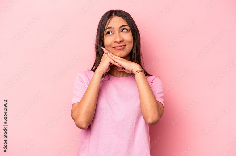 Young hispanic woman isolated on pink background keeps hands under chin, is looking happily aside. Young hispanic woman isolated on pink background keeps hands under chin, is looking happily aside.