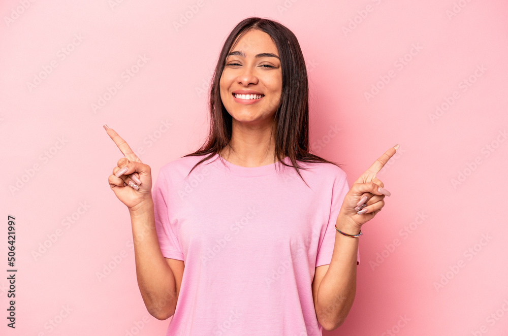 Young hispanic woman isolated on pink background indicates with both fore fingers up showing a blank space. Young hispanic woman isolated on pink background indicates with both fore fingers up showing a blank space.