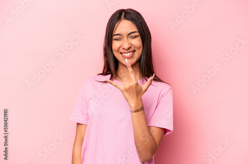 Young hispanic woman isolated on pink background showing rock gesture with fingers