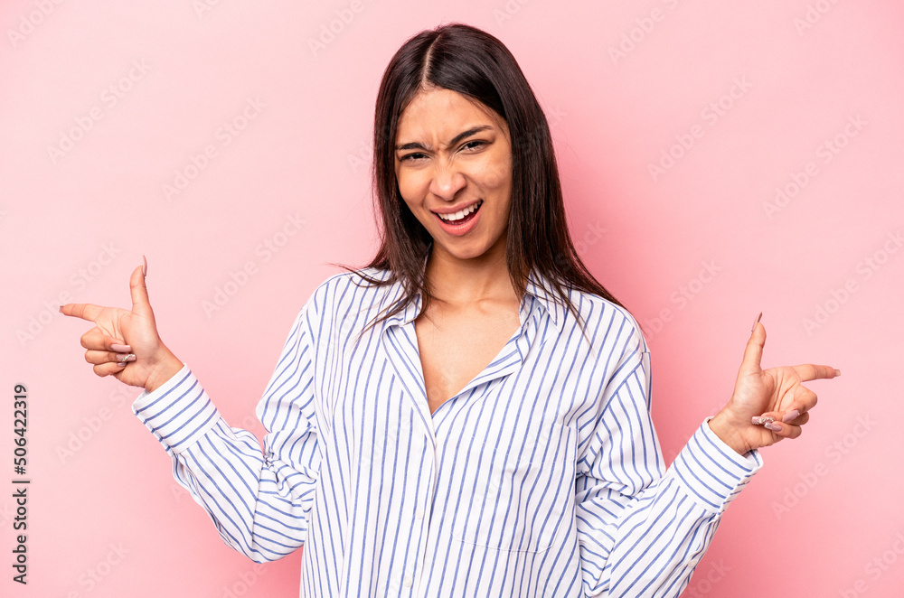 Young hispanic woman isolated on pink background pointing to different copy spaces, choosing one of them, showing with finger. Young hispanic woman isolated on pink background pointing to different copy spaces, choosing one of them, showing with finger.