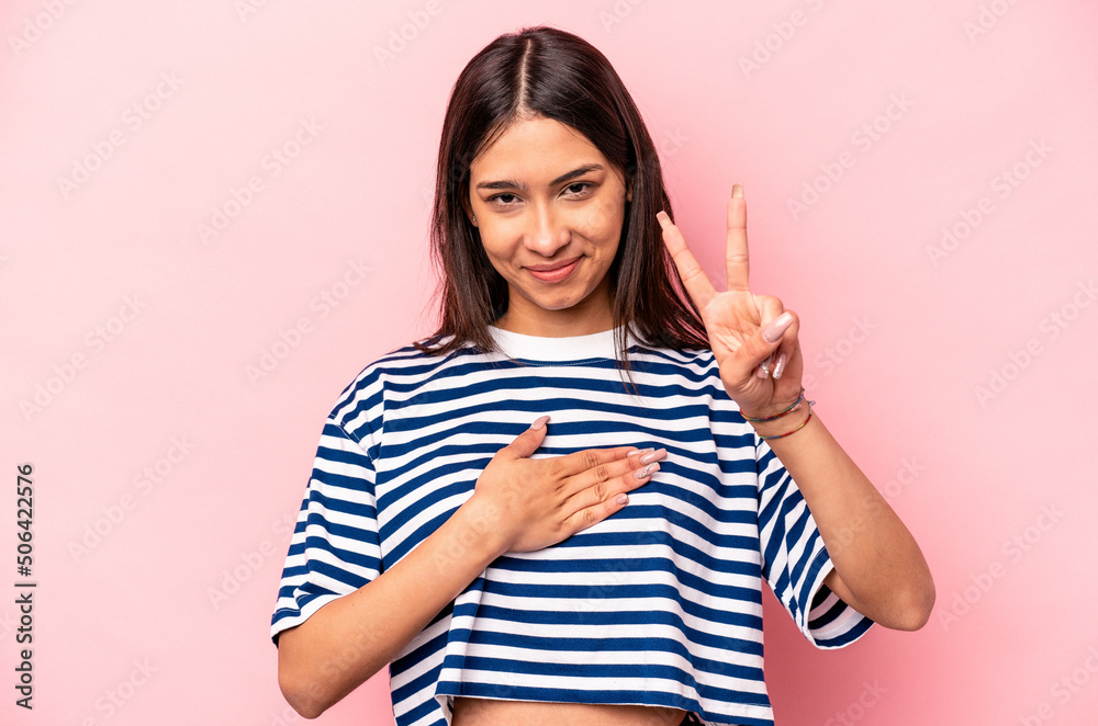 Young hispanic woman isolated on pink background taking an oath, putting hand on chest.