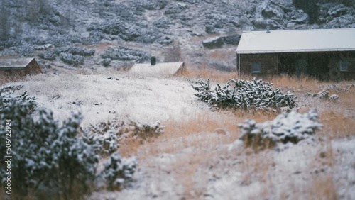 Light first snow falls on the withered grass, stones, and roofs of the wooden cabins. Slow-motion. photo