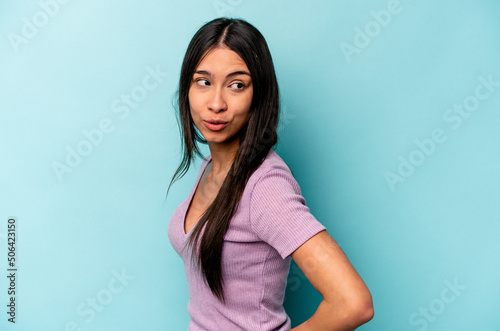 Young hispanic woman isolated on blue background looks aside smiling, cheerful and pleasant.