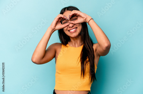 Young hispanic woman isolated on blue background showing okay sign over eyes