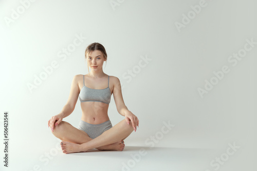 Portrait of attractive young woman sitting on floor in underwear, posing isolated over grey studio background. Meditation