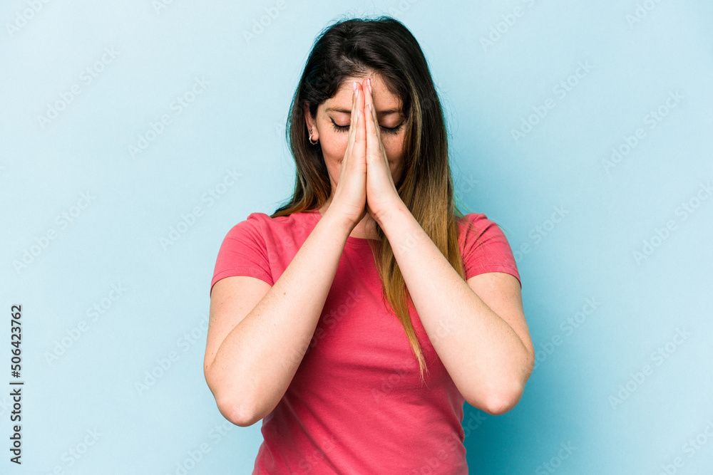 Young caucasian woman isolated on blue background holding hands in pray near mouth, feels confident. Young caucasian woman isolated on blue background holding hands in pray near mouth, feels confident.