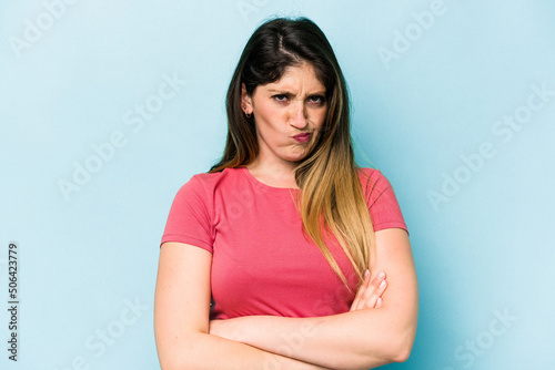 Young caucasian woman isolated on blue background frowning face in displeasure, keeps arms folded.