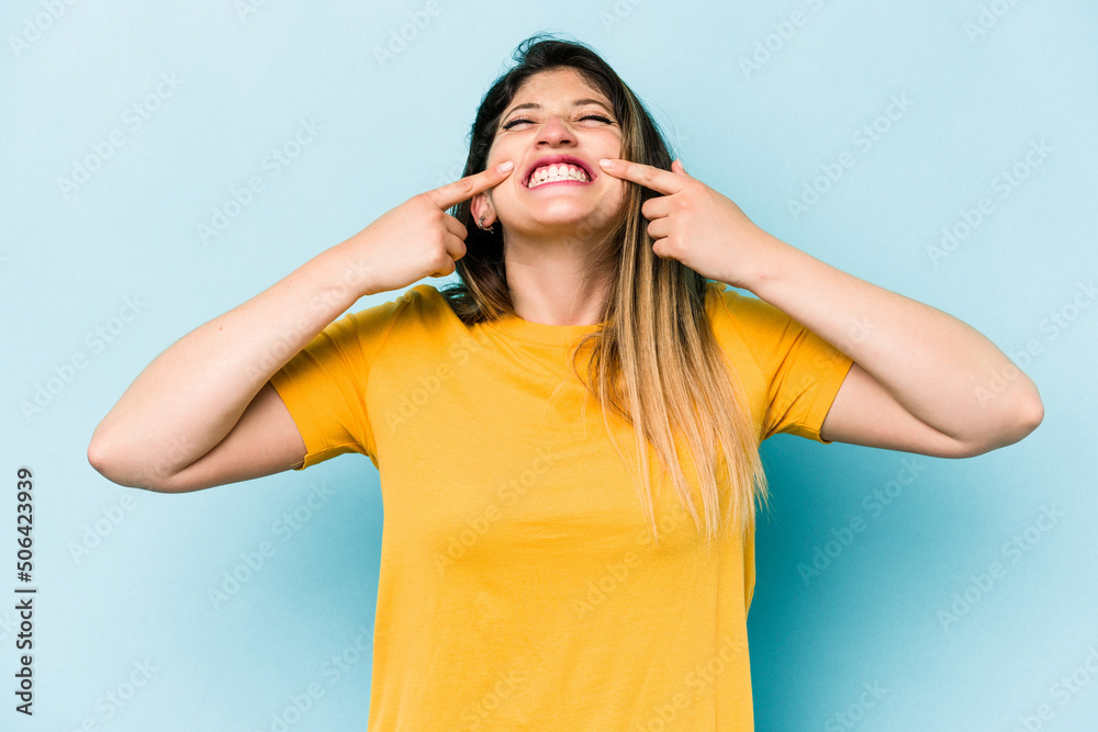 Young caucasian woman isolated on blue background smiles, pointing fingers at mouth. Young caucasian woman isolated on blue background smiles, pointing fingers at mouth.