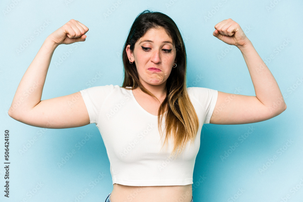 Fototapeta premium Young caucasian woman isolated on blue background showing strength gesture with arms, symbol of feminine power