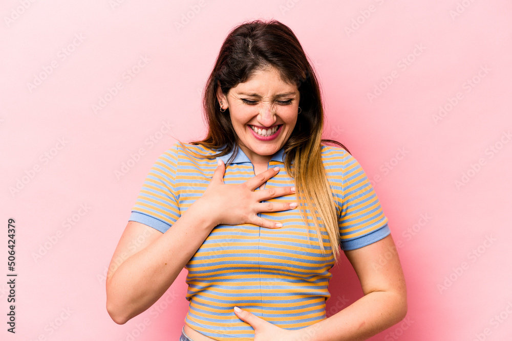 Young caucasian woman isolated on pink background laughs happily and has fun keeping hands on stomach.