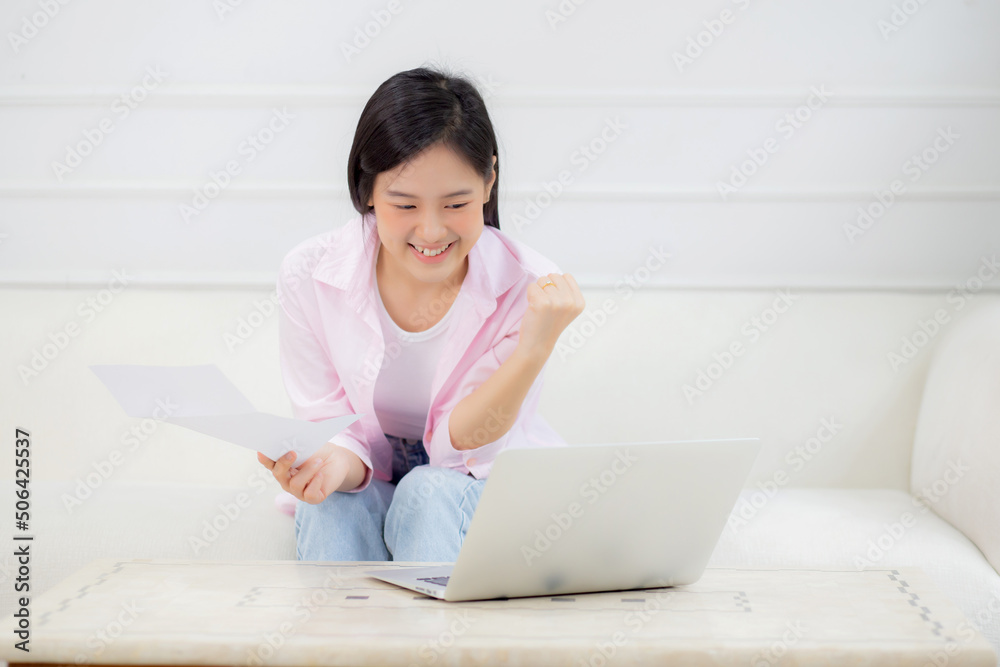 Young asian business woman working on laptop computer and looking graph and chart of report for profit on paper while success at home, businesswoman looking investment and income, data of infographic.