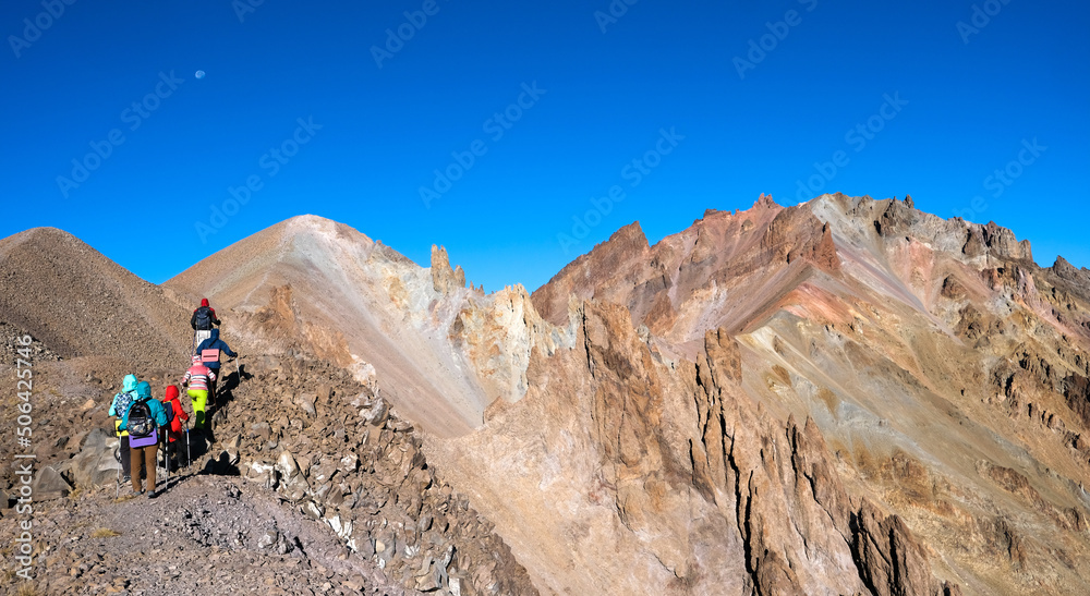 Group of hikers climbing stony mountains in daytime, panorama