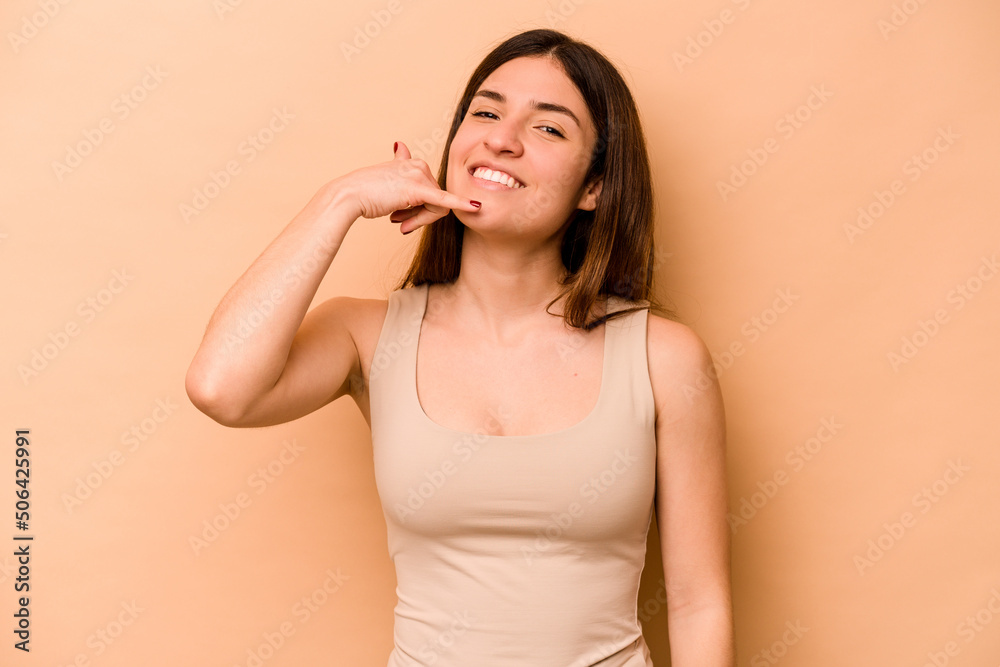 Young hispanic woman isolated on beige background showing a mobile phone call gesture with fingers. Young hispanic woman isolated on beige background showing a mobile phone call gesture with fingers.