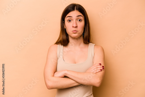 Young hispanic woman isolated on beige background shrugs shoulders and open eyes confused.