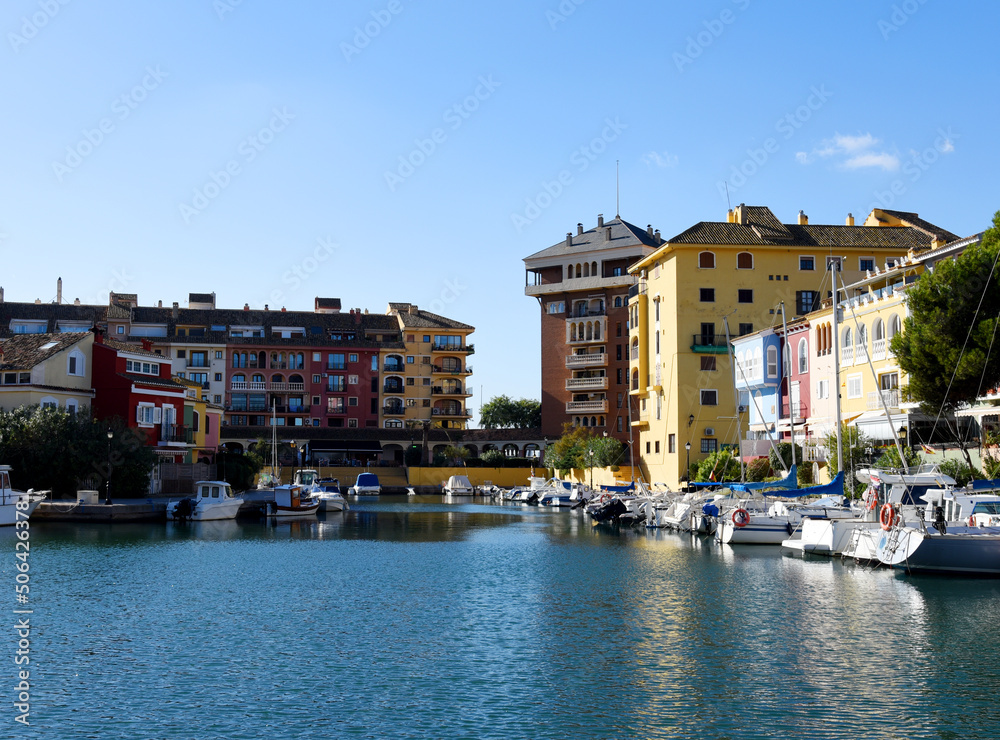 Jetty with yacht. Yachts and motor boats in marina Port Saplaya, Valencia. Yacht and fishing motorboat in yacht club. Colourful houses with apartments at coast Mediterranean Sea. Sailboat near pier.