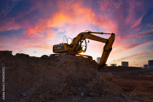 Excavator on earthmoving on sunset background. Loader at open pit mining. Excavator digs gravel in quarry. Heavy construction equipment on excavation. Earth mover ar construction site. Open-pit mine.