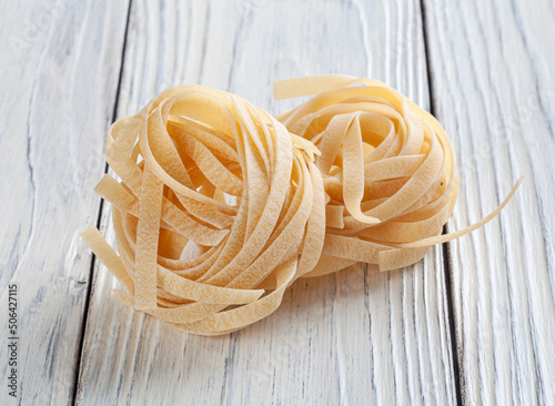 Uncooked tagliatelle pasta on white wooden table