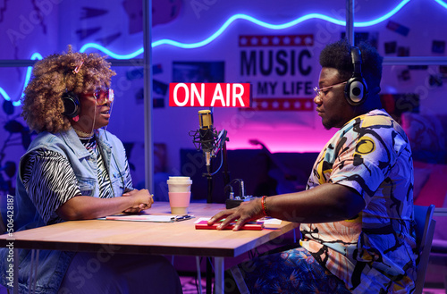 Young gen Z African American man and woman sitting in front of each other recording podcast or doing radio broadcasting in studio at home photo