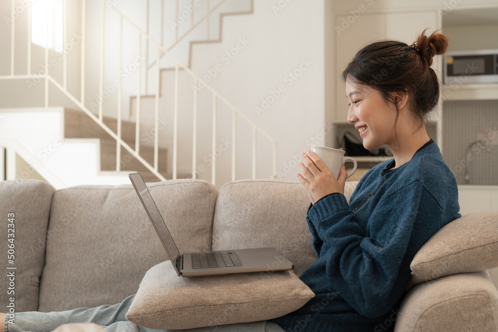 Calm young asian female working at laptop sitting on sofa, happy girl browsing internet or shopping online during sunny weekend at home, relaxing on couch with computer. Calm young asian female working at laptop sitting on sofa, happy girl browsing internet or shopping online during sunny weekend at home, relaxing on couch with computer.