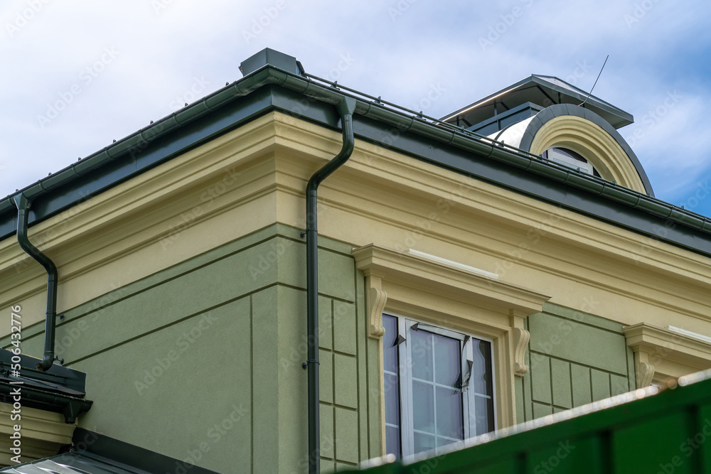 Corner of house with windows, new green metal tile roof and rain gutter. Metallic Guttering System, Guttering and Drainage Pipe Exterior