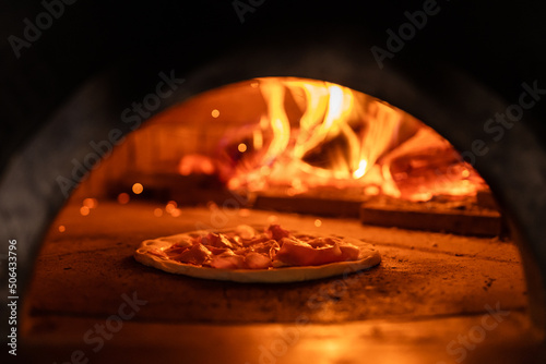 Pizza concept. Preparing traditional italian pizza. Long shovel for pizza, baking dough in a professional oven with open fire in interior of modern restaurant kitchen