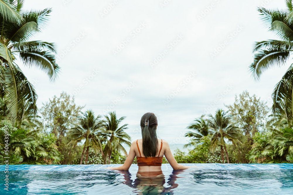 Behind woman wearing swimsuit look out beautiful view and relaxing in tropical swimming pool at spa resort. Female relaxation on vacation in summer.
