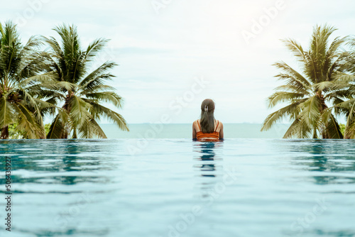 Female relaxation on vacation in summer. Behind woman happiness wearing swimsuit look out beautiful view and relaxing in tropical swimming pool at spa resort.