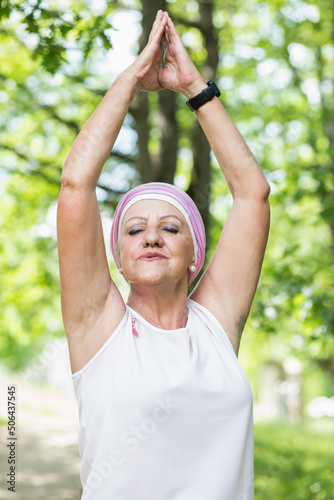 senior woman with breast cancer practices yoga in the forest
